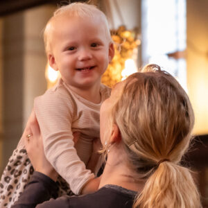 Lille barn smiler og løftes op af sin mor, der står med ryggen til