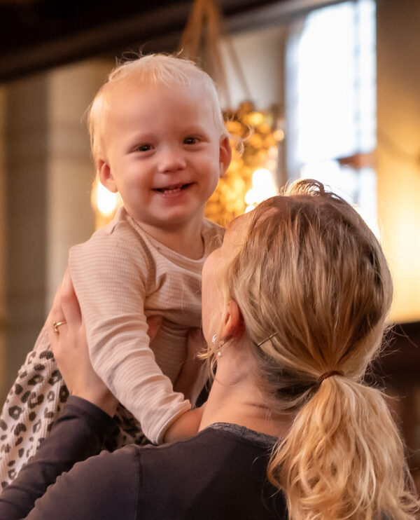 Lille barn smiler og løftes op af sin mor, der står med ryggen til